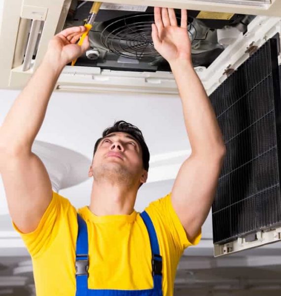 Man on yellow shirt fixing air conditioner — Air Conditioning on the Sunshine Coast, QLD